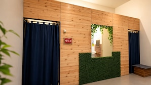 A room with wooden panel walls, a mirror with a green leafy frame, a blue curtain, and a small bench. - Nusantara Tajur Bogor Hostel By Reccoma (Bogor)