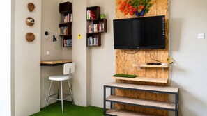 A room with a TV, bookshelves, a desk, a chair, and a small plant.