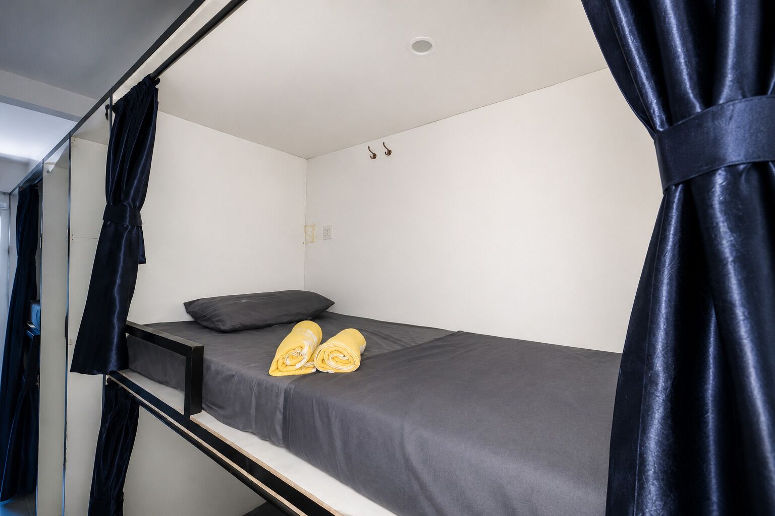 A bunk bed with a black mattress and a single pillow, a small shelf, and a pair of yellow towels.