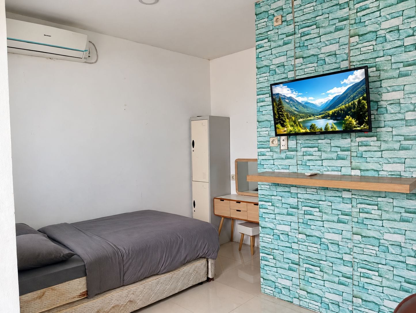 Un dormitorio con cama, escritorio, armario y televisor montado en una pared con diseño de piedra.