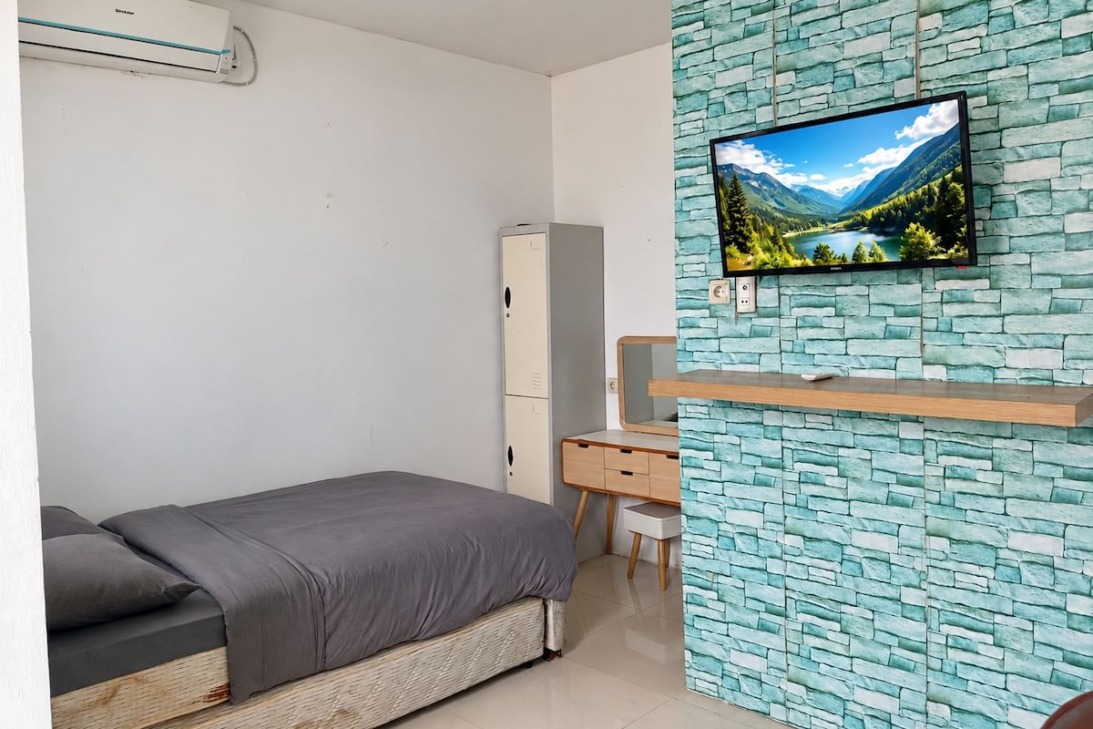 Un dormitorio con cama, escritorio, armario y televisor montado en una pared con diseño de piedra.