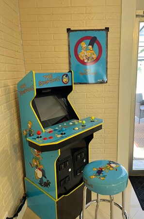 A The Simpsons arcade machine with a blue seat and a poster of the show on the wall.