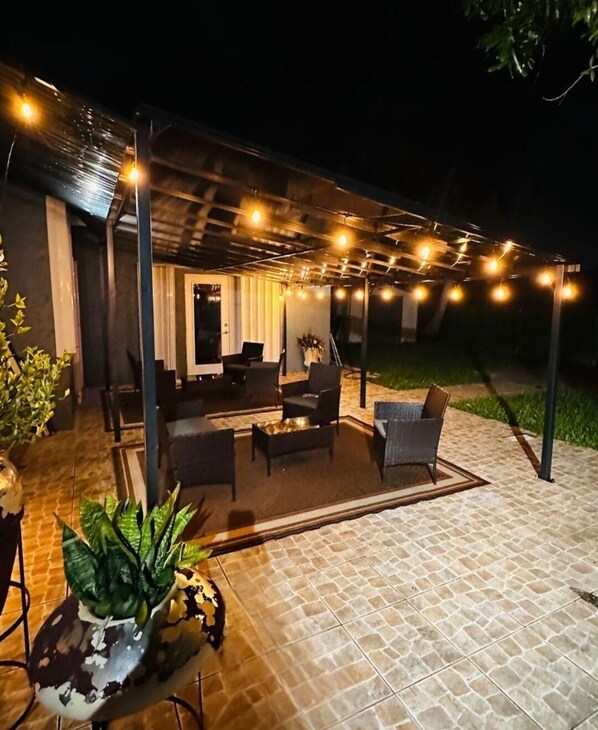 An outdoor patio with a covered seating area, string lights, and a potted plant.