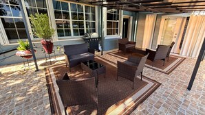 Eine Terrasse im Freien mit Korbmöbeln, einem Grill und Kübelpflanzen.
