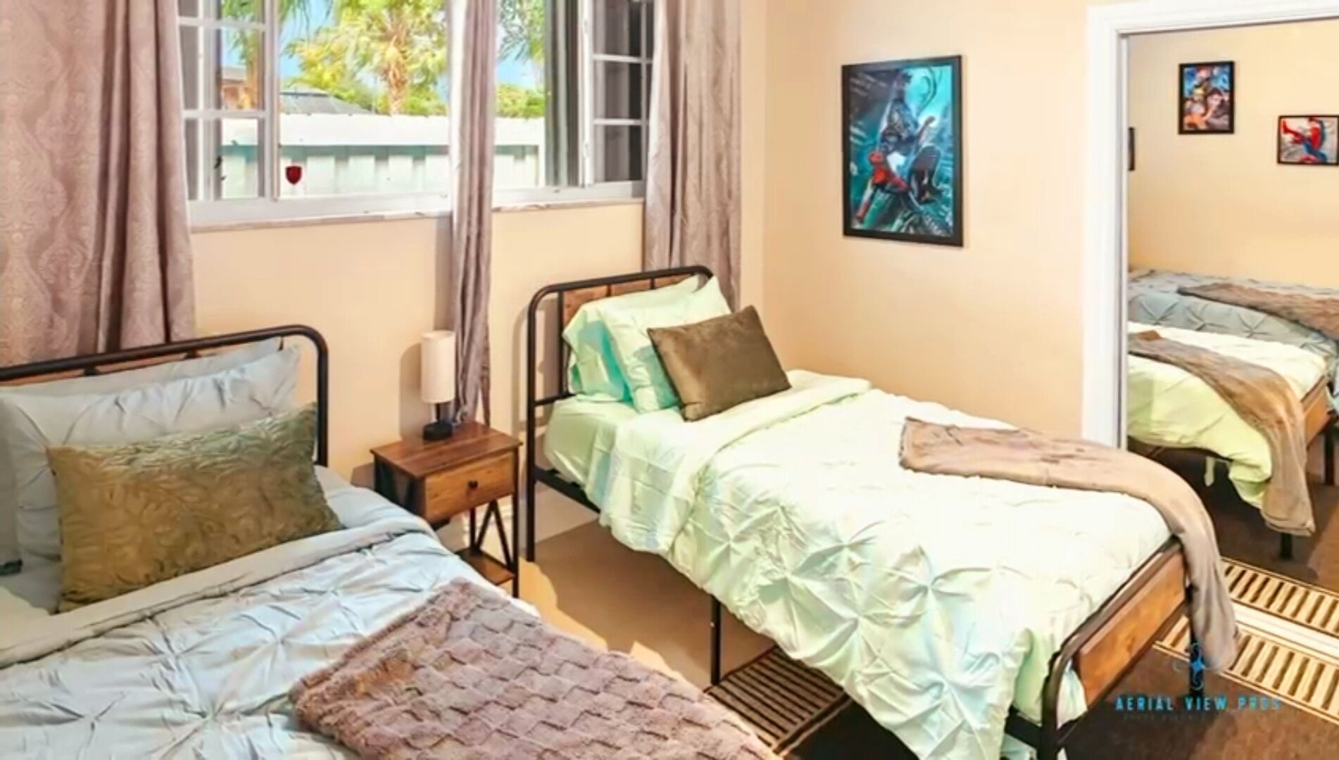 Un dormitorio con dos camas, una ventana con cortinas, una mesita de noche con lámpara y una pared con cuadros enmarcados.
