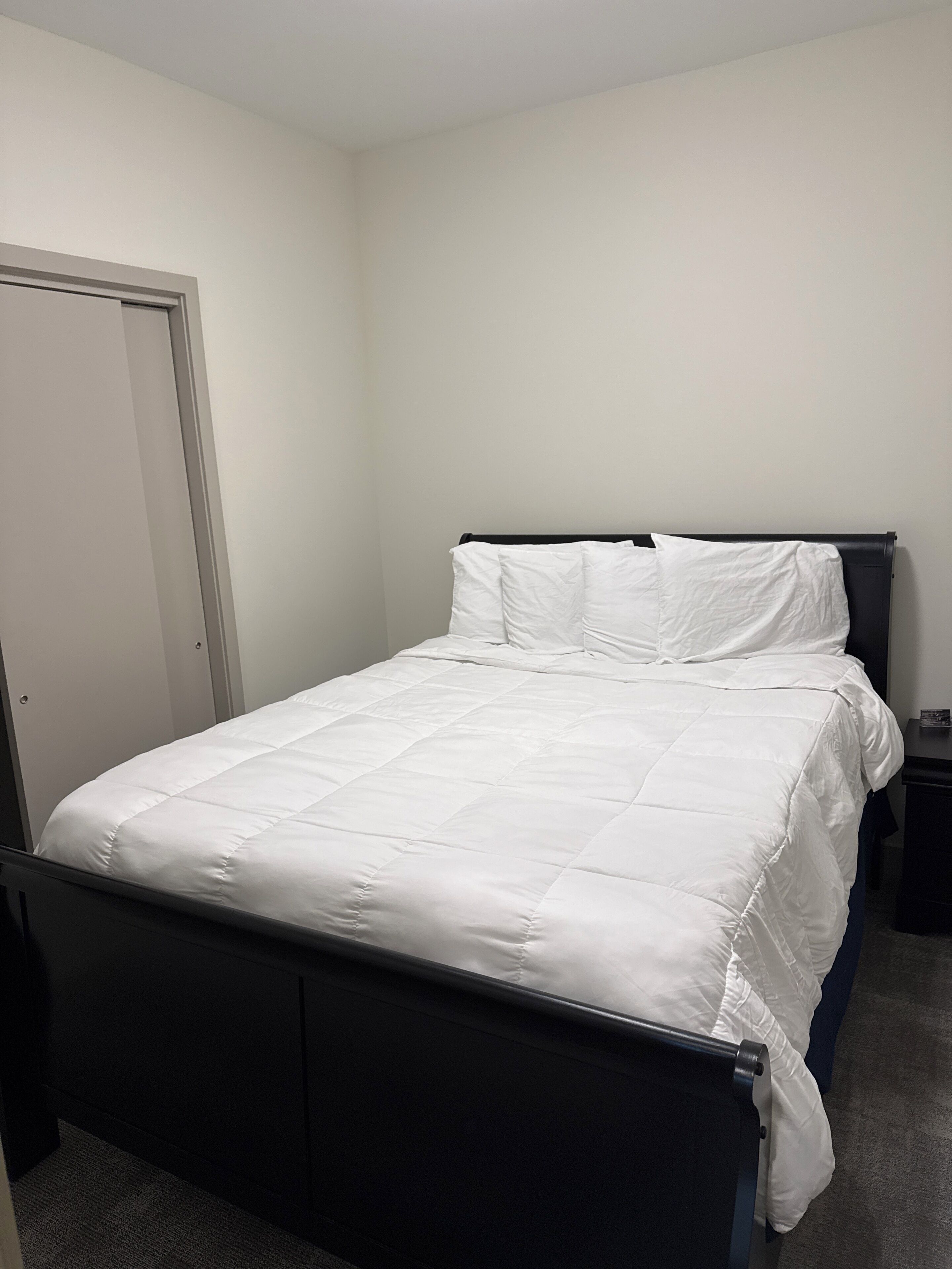 A neatly made bed in a room with a closed door and a small bedside table.