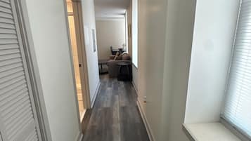 Un pasillo estrecho con suelo de madera, paredes blancas y una ventana a la derecha.