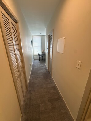A hallway with a carpeted floor, a door with louvered shutters, and a wall-mounted light switch. - Hilliard Lofts (Cleveland)
