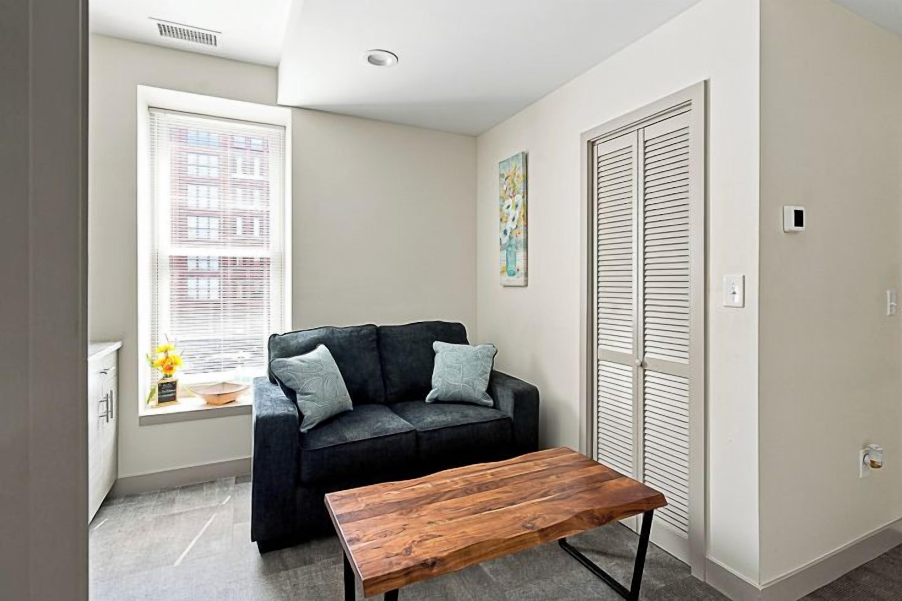 A room with a sofa, a coffee table, a window with blinds, a painting on the wall, and a closet with louvered doors.