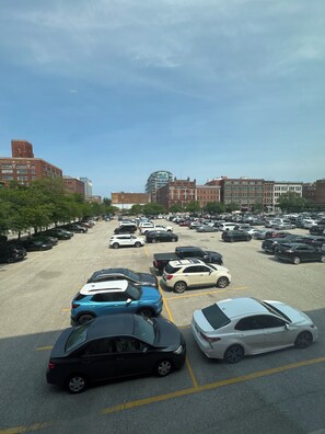 Ein Parkplatz mit mehreren Autos, Gebäuden im Hintergrund und Bäumen entlang der Straße.