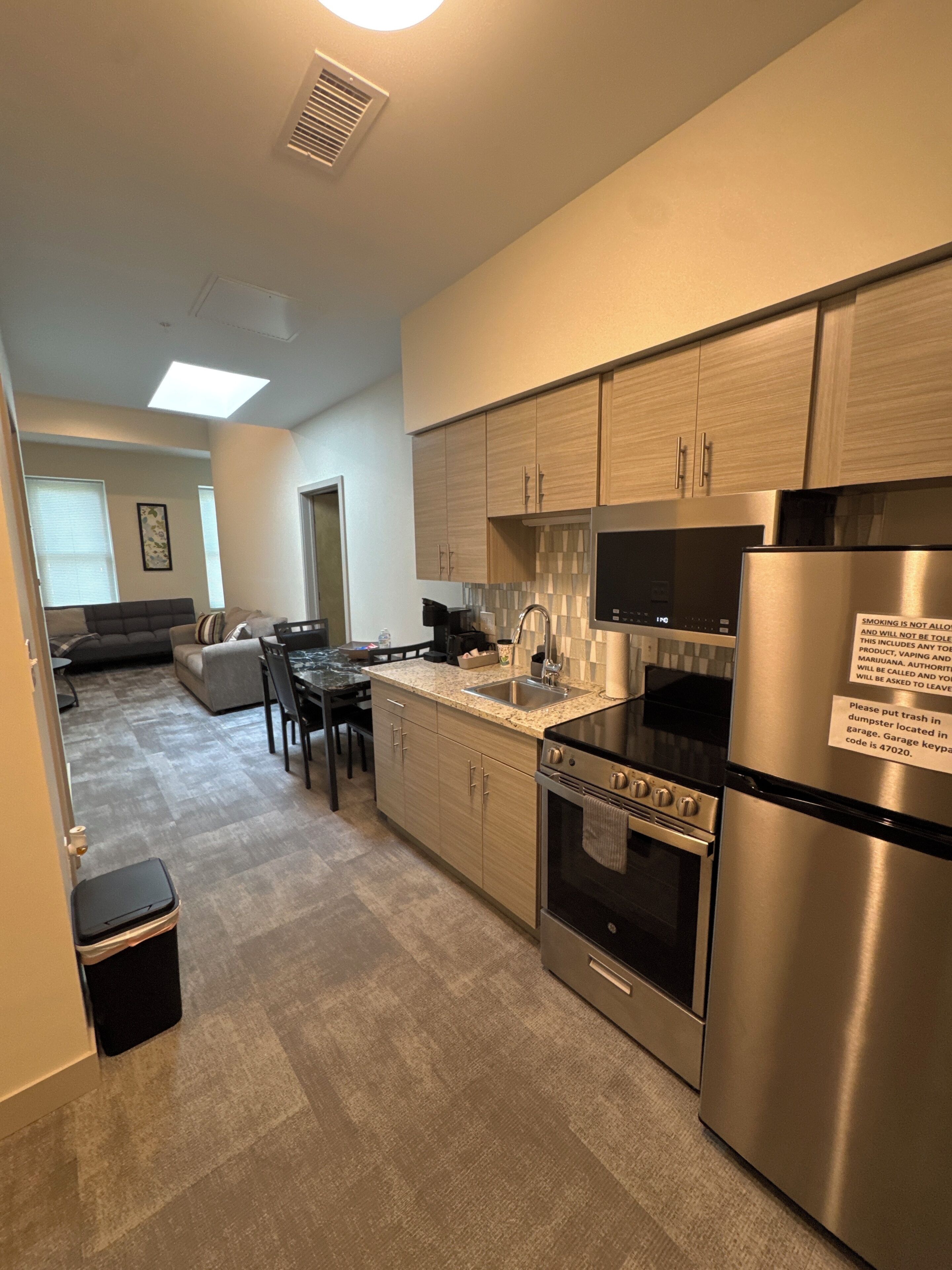 A modern kitchen with stainless steel appliances, a dining area with a table and chairs, and a living room with a sofa and a coffee table.