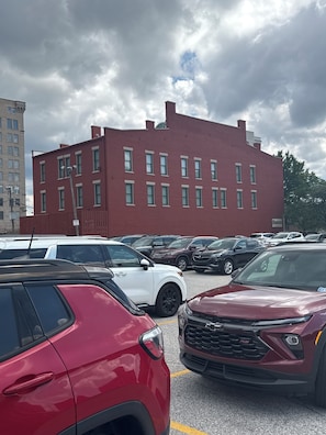 Un estacionamiento con varios SUV, un edificio de ladrillo rojo al fondo y un cielo nublado.