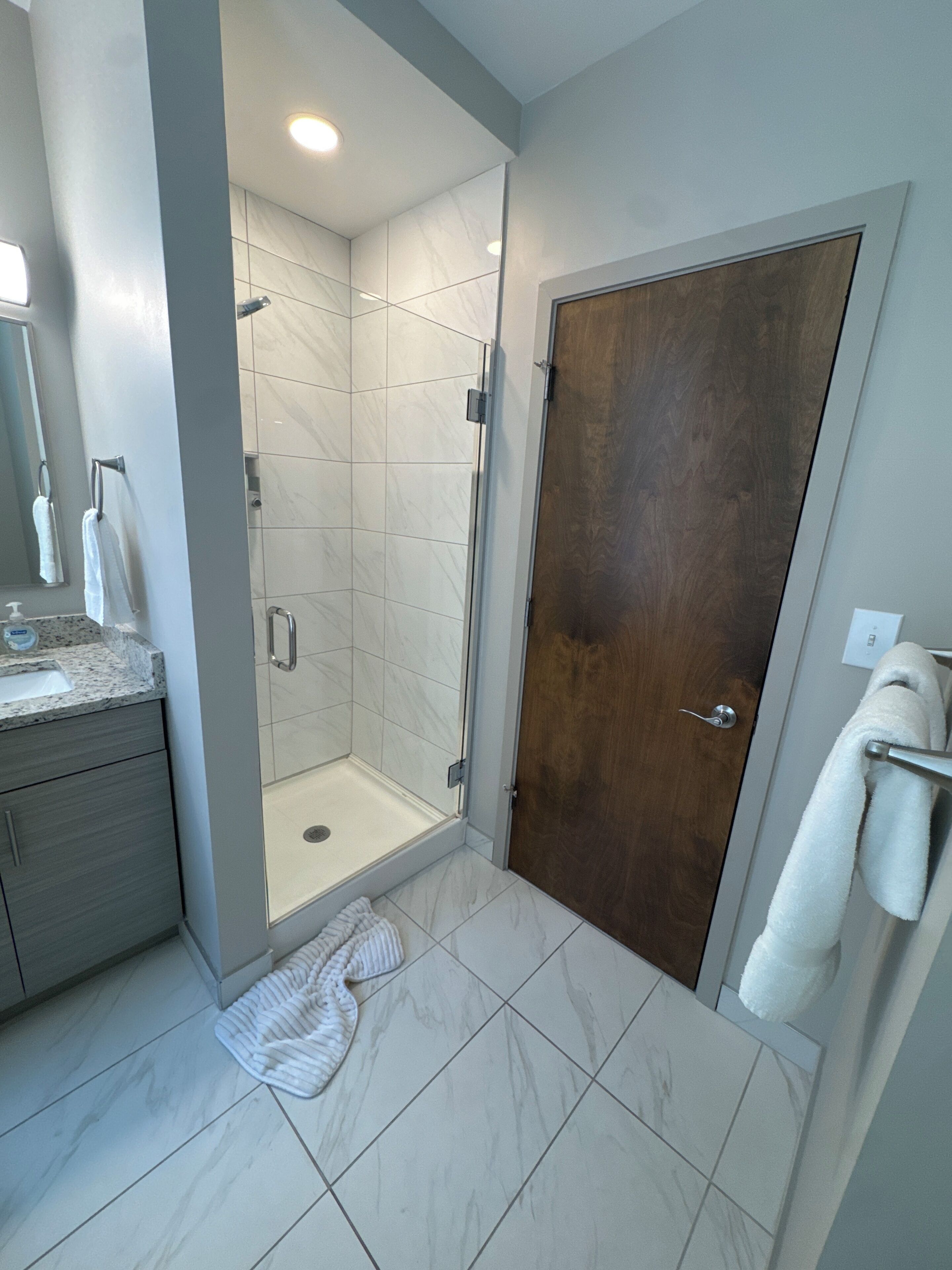 Un baño con ducha, lavamanos, espejo y puerta.