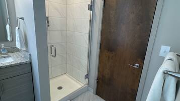 Un baño con ducha, lavamanos, espejo y puerta.