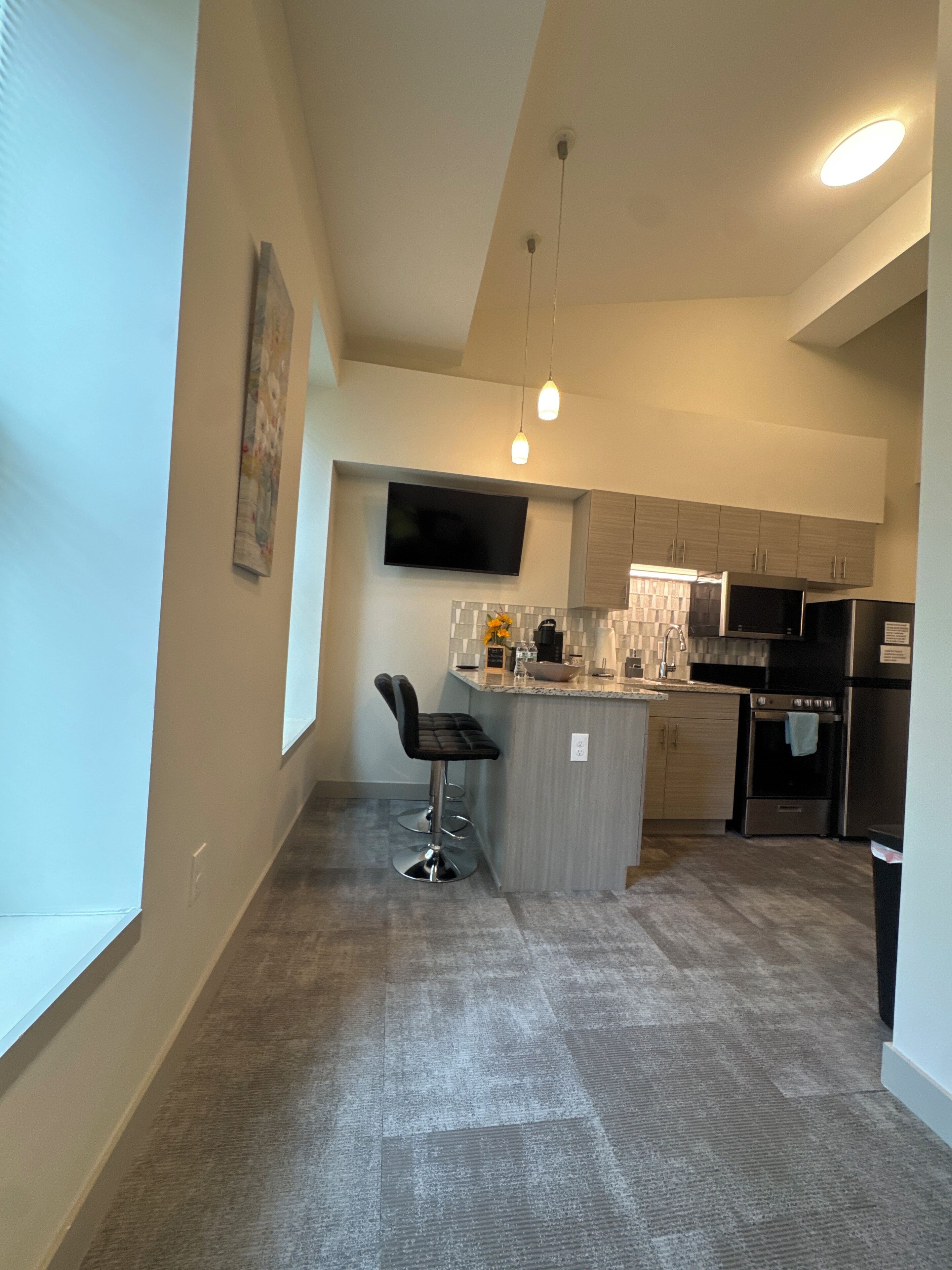 Cocina moderna con televisión de pantalla plana, electrodomésticos de acero inoxidable y una barra con taburetes.