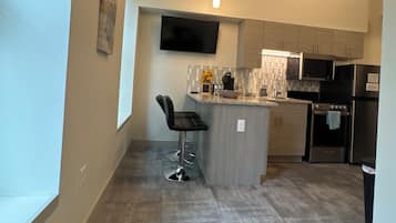 Cocina moderna con televisión de pantalla plana, electrodomésticos de acero inoxidable y una barra con taburetes.