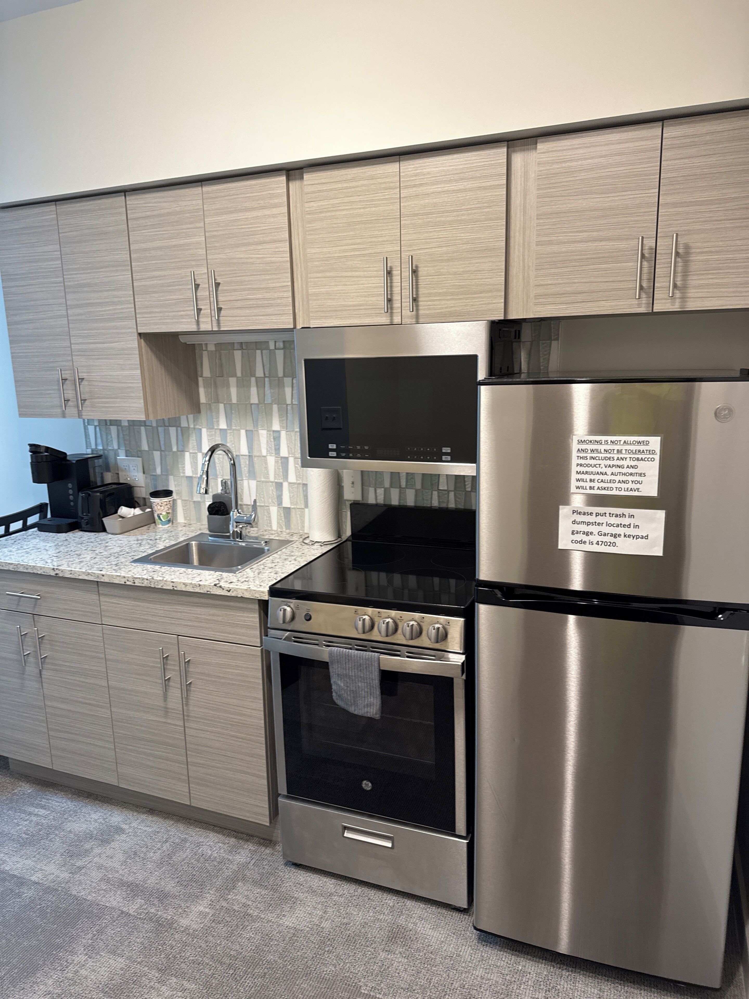 A modern kitchen with stainless steel appliances, a tiled backsplash, and wooden cabinets.