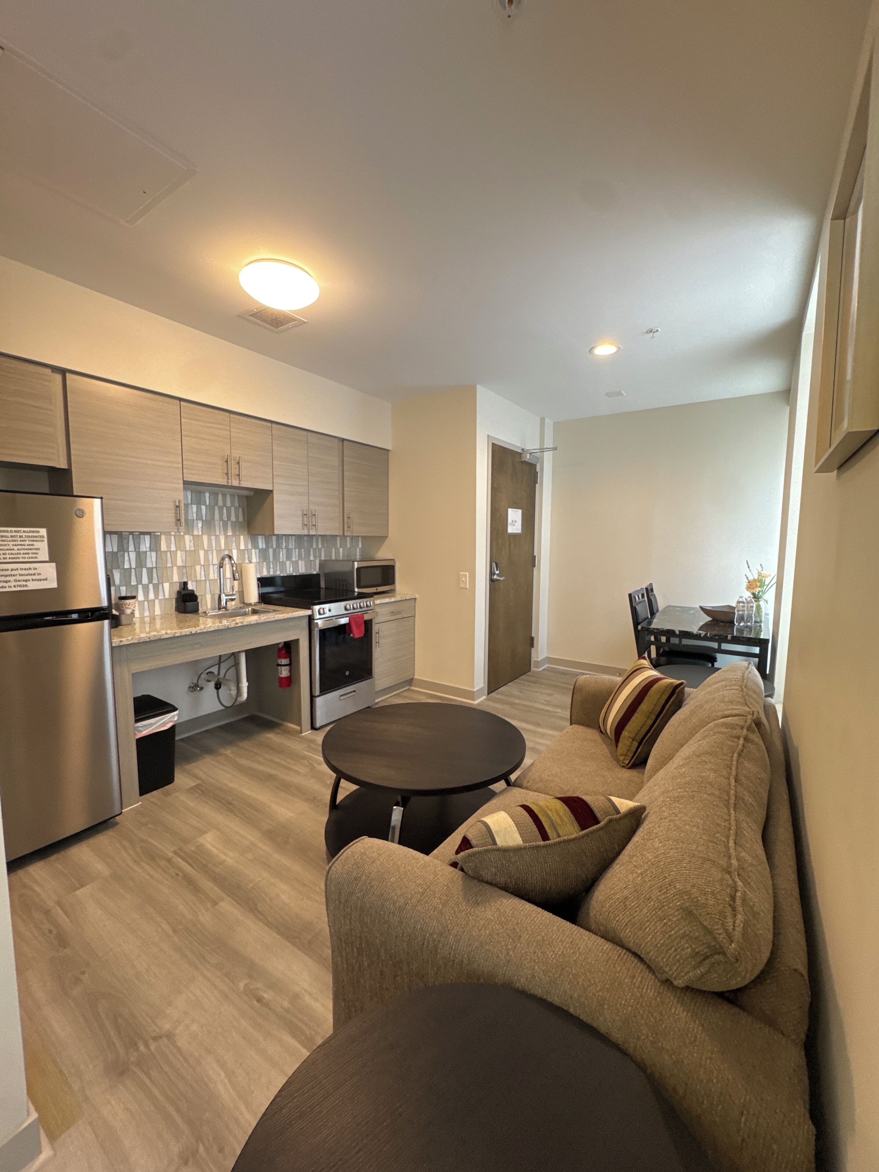 A modern kitchen with stainless steel appliances, a dining area with a table and chairs, and a living room with a sofa and a coffee table.
