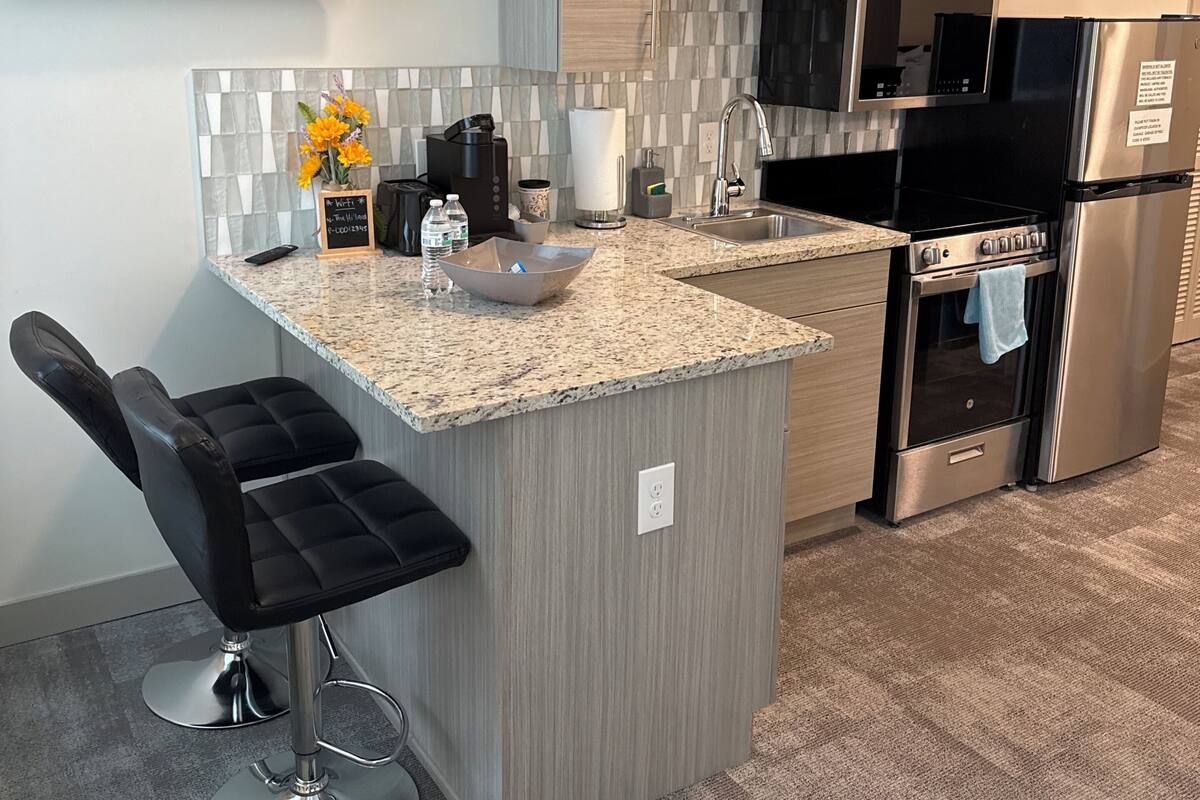 A modern kitchen with a granite countertop, stainless steel appliances, and a bar stool.