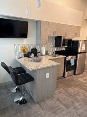 A modern kitchen with a granite countertop, stainless steel appliances, and a bar stool. - Hilliard Lofts (Cleveland)