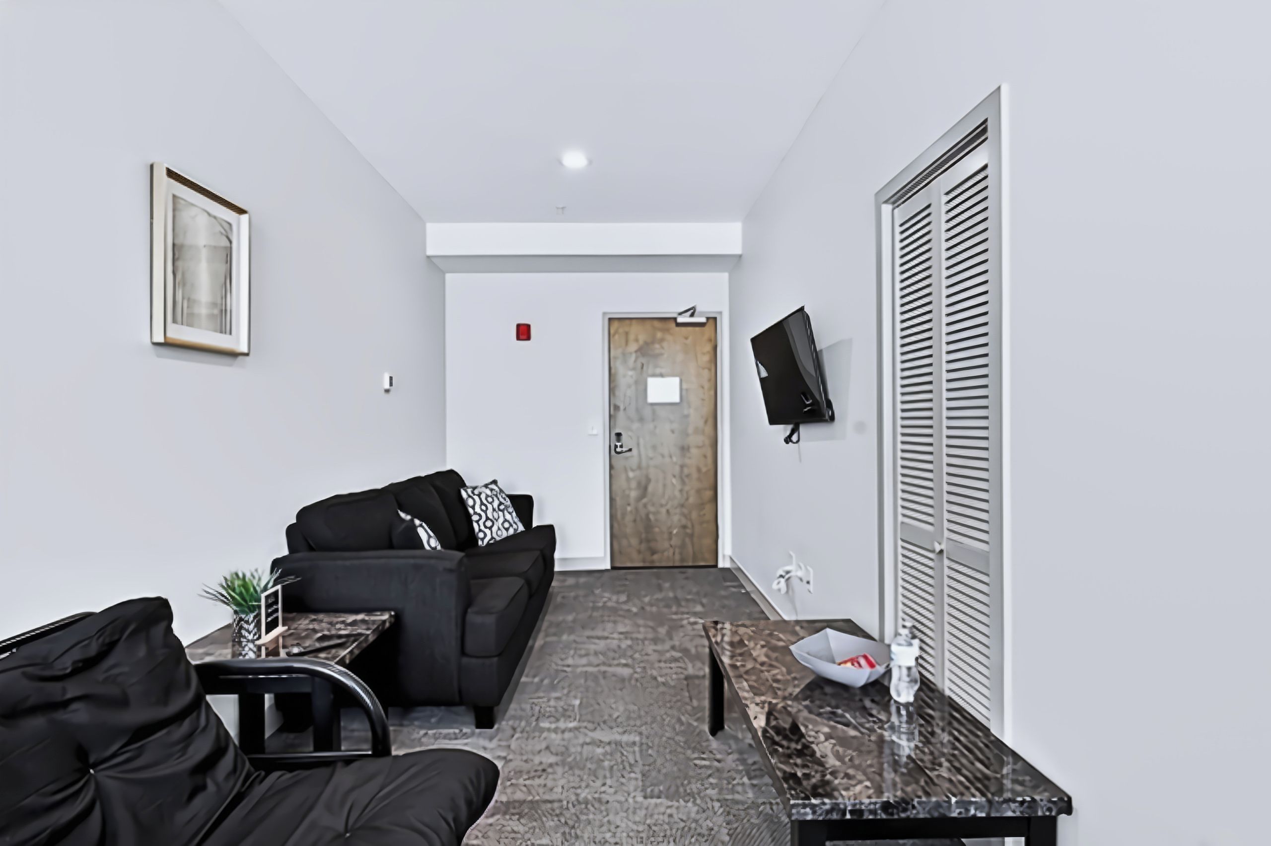 Eine moderne Hotelhalle mit einer Couch, einem Couchtisch, einem an der Wand befestigten Fernseher und einer Tür im Hintergrund.
