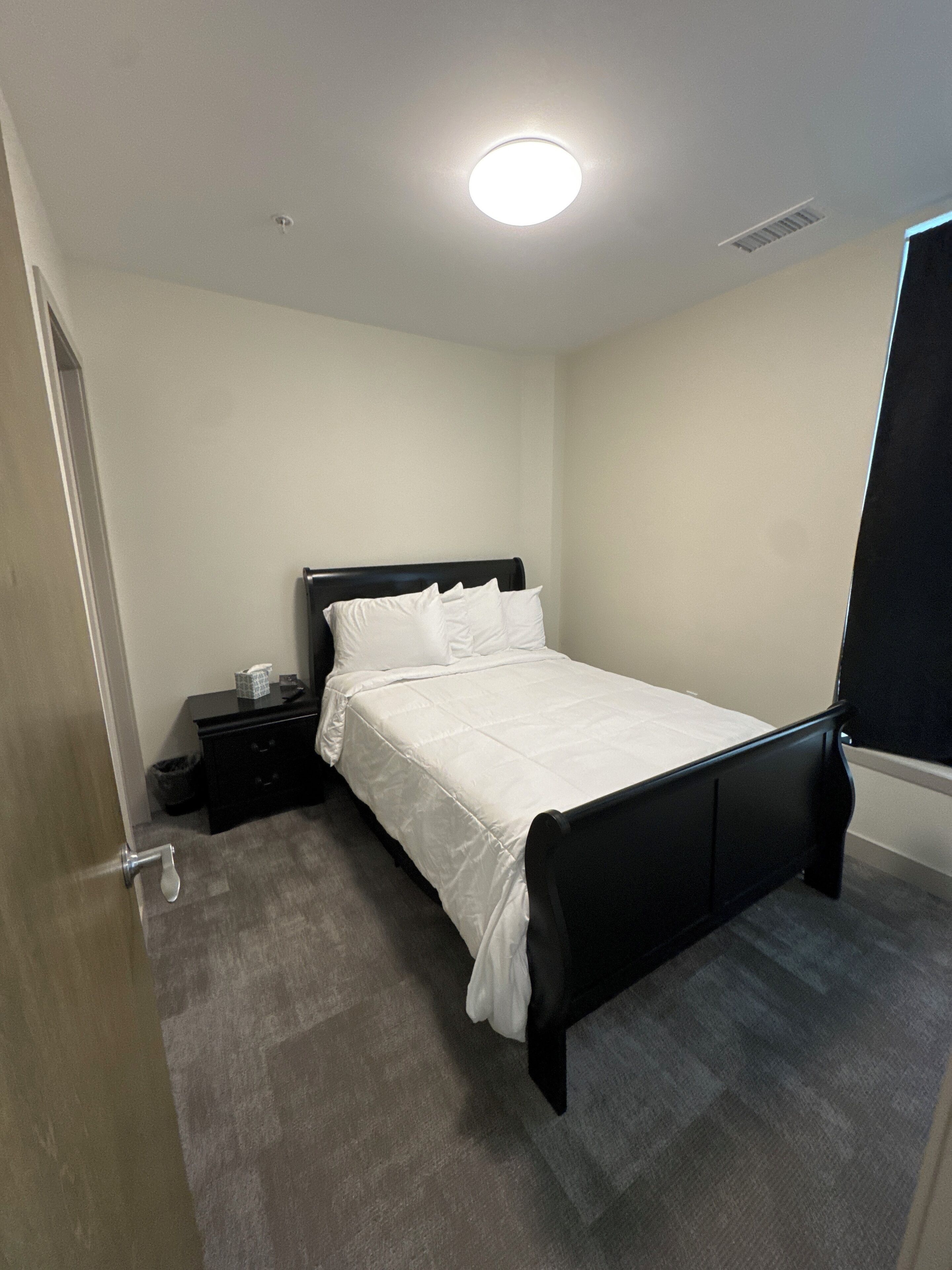A bedroom with a bed, a nightstand, a dresser, and a door.