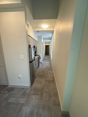 A narrow hallway with a kitchen area on the left, featuring a refrigerator and cabinets. - Hilliard Lofts (Cleveland)