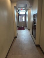 Un pasillo con piso de baldosas, alfombra roja, una puerta con ventanal y una caja fuerte instalada en la pared.