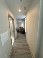 A hallway with a marble wall, a dining area with a table and chairs, and a light fixture on the ceiling.