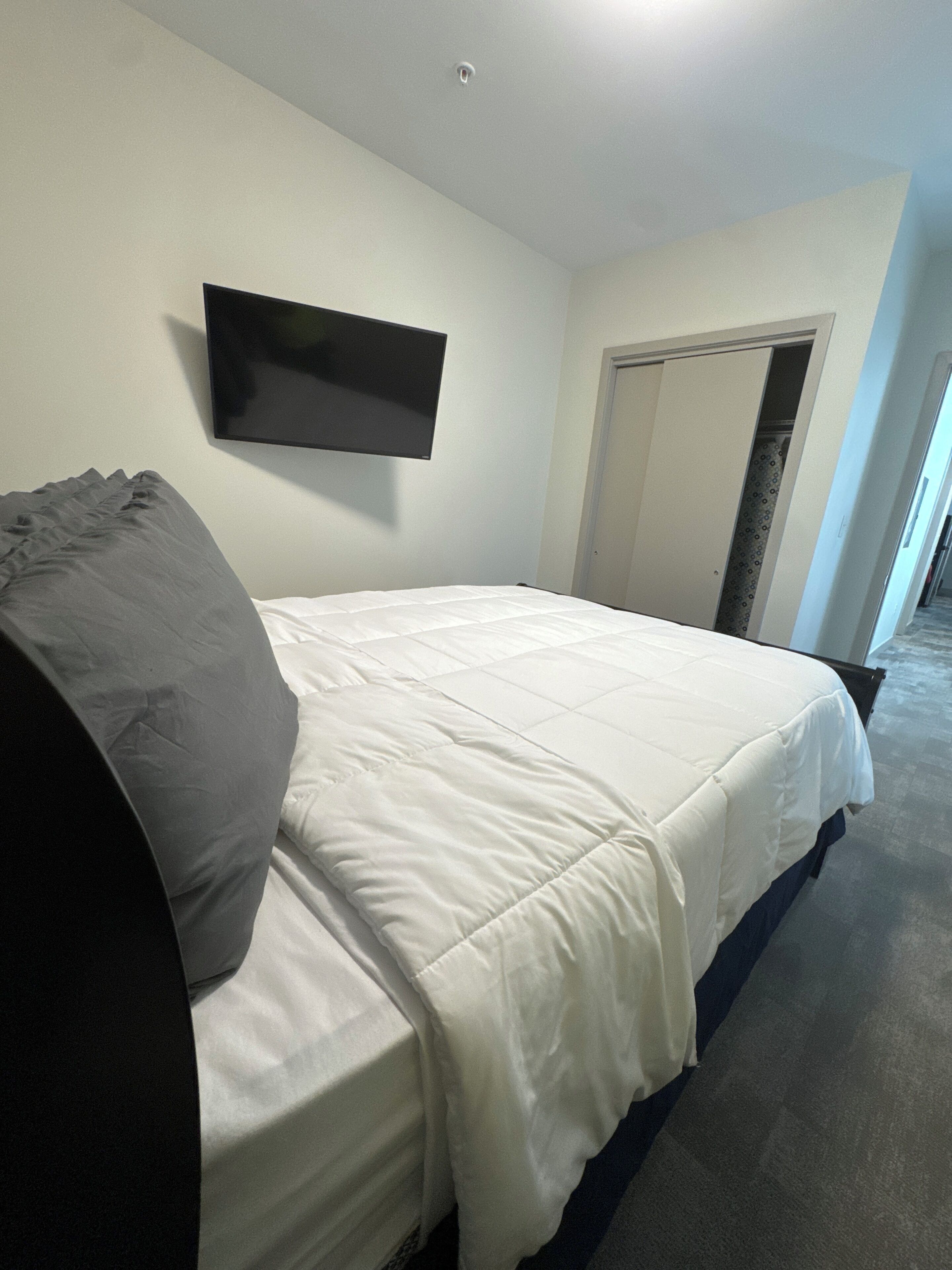 Un dormitorio con cama, televisor de pantalla plana en la pared y puerta que da a otra habitación.