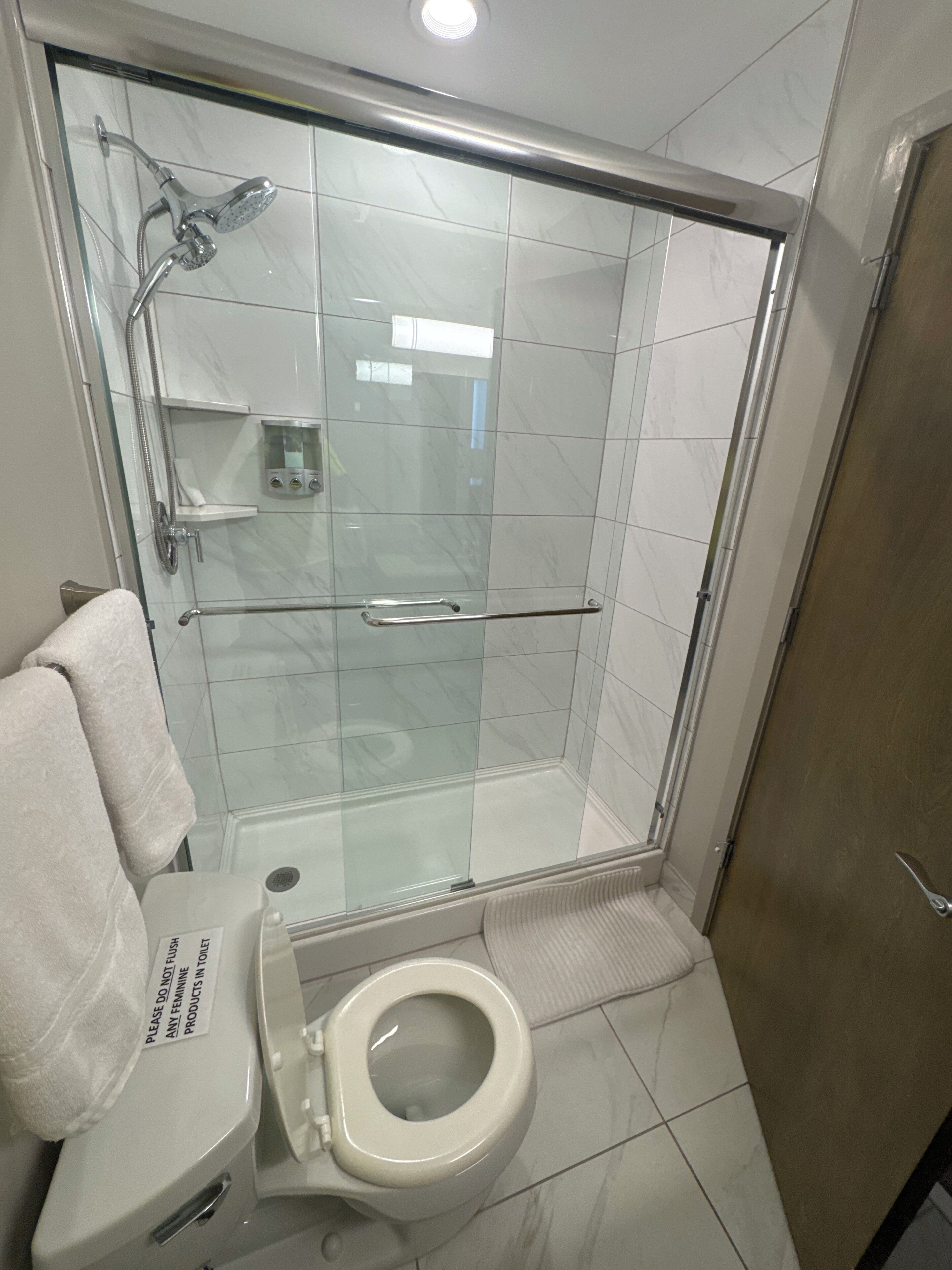 Un baño moderno con ducha envuelta en vidrio, inodoro y mampara de vidrio.