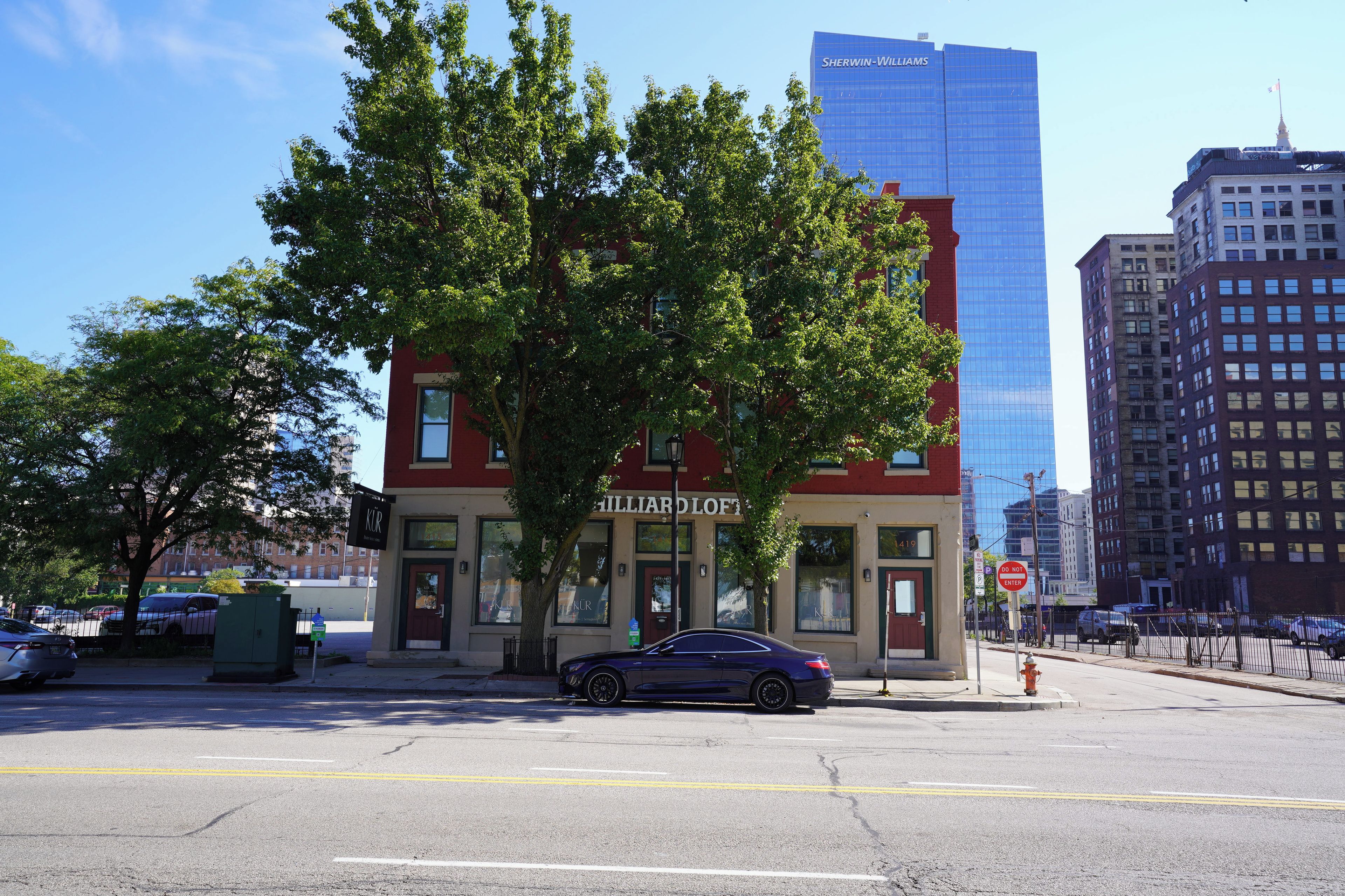 A building with a large tree in front, a parking sign, and a 'Do Not Enter' sign on the street.