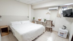 Un dormitorio con cama, una silla, un escritorio, una estantería con plantas y un aire acondicionado.