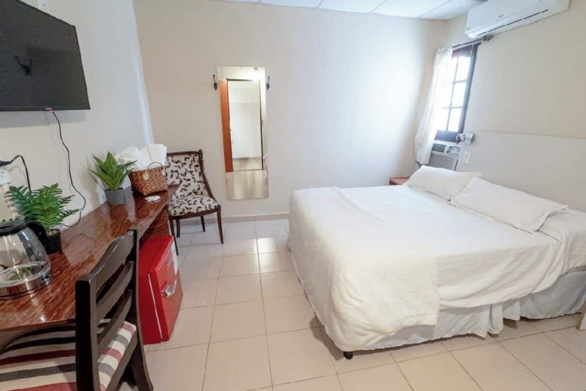 Una habitación de hotel con cama, escritorio, silla, espejo y televisor.