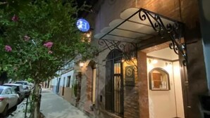 Un edificio con fachada de piedra, una entrada visible y un letrero con una 'H' azul que indica un hotel.