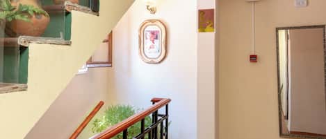 A staircase with a wooden handrail, a framed picture on the wall, and a fire alarm on the right.