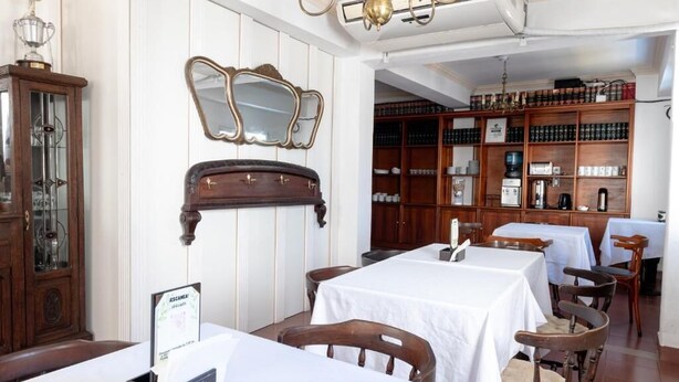 Un área de comedor con mesas, sillas, un armario de madera y un espejo en la pared.