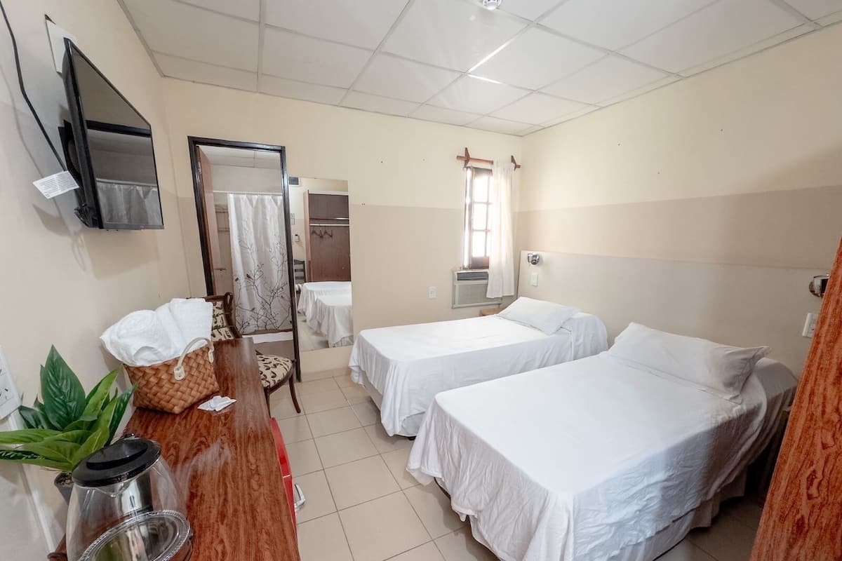 Habitación de hotel con dos camas, un escritorio con hervidor, una silla, un televisor y una ventana con cortinas.