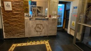 Un área de recepción con pared de piedra, candelabro, mostrador de recepción con logotipo 'HSL' y alfombra estampada.