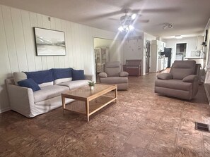 A living room with a sofa, armchairs, a coffee table, and a kitchen in the background.