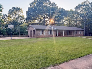 A brick building with a covered porch, a basketball court, and a well-maintained lawn.