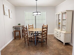 Uma área de refeições com uma mesa redonda, cadeiras de madeira, um armário e uma janela com persianas.