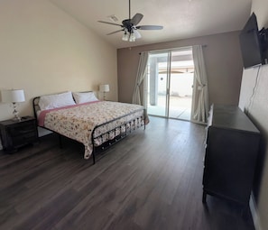 Una camera da letto con un letto, comodini, una ventola a soffitto, una scrivania e un'ampia finestra con tende.