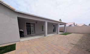 Un patio coperto con pavimento in cemento, una porta scorrevole in vetro e un piccolo angolo salotto esterno.