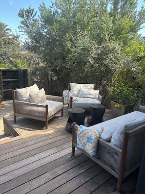 Eine Terrassenausstattung mit Korbmöbeln, darunter eine Couch und eine Liege, umgeben von Grünpflanzen und einem Holzboden.
