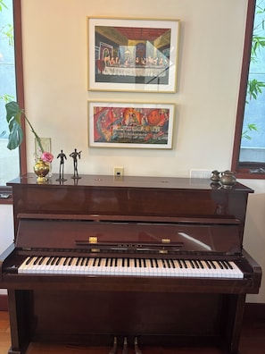 Ein Klavier mit Kawai-Logo, zwei gerahmte Kunstwerke an der Wand, eine Vase mit Pflanze und ein dekorativer Gegenstand auf der Oberseite des Klaviers.