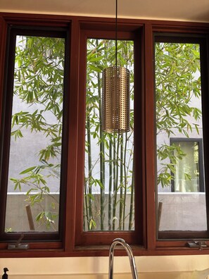 Ein Fenster mit einem Metallarmaturen, einer Pendelleuchte und Bambuspflanzen davor.