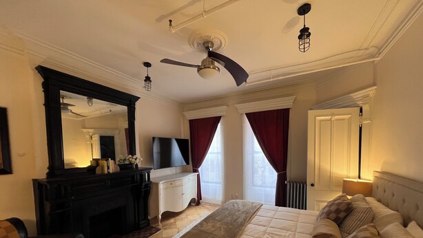 A bedroom with a bed, a dresser, a mirror, a ceiling fan, and a window with curtains. - Peaceful 1-bedroom suite in boutique guesthouse with AC in vibrant New York (New York)