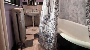 A bathroom with a checkered floor, a white bathtub, a shower curtain with floral patterns, a sink, and a mirror. - Peaceful 1-bedroom suite in boutique guesthouse with AC in vibrant New York (New York)