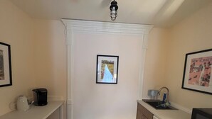 A small kitchen with a white cabinet, a sink, a coffee maker, and a framed picture on the wall. - Peaceful 1-bedroom suite in boutique guesthouse with AC in vibrant New York (New York)